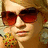 Pixelated close-up of a person wearing large red-tinted sunglasses and a colorful patterned top with yellow, red, and green hues.