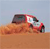 Pixelated red vehicle with dark roof on brown terrain under light blue sky, static image with no visible text or motion.