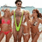 Four people stand together on a beach; one wears a red bikini top, another a green swimsuit, and two others wear white swimwear.