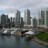 Pixelated cityscape with tall buildings reflected in water, green grassy area on right, overcast sky.