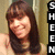 A pixelated image of a person with long brown hair and light skin, wearing a dark top against a beige background.