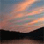 A static pixelated image of a sunset sky with orange and pink clouds over a dark silhouette of land and water.