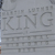 Pixelated grayscale image with large stylized text 'KING' centered, surrounded by smaller indistinct text elements and horizontal lines on a light gray background.
