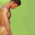 Static pixelated image of a shirtless man with dark hair standing against a green background, viewed from the side in profile.