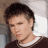 A pixelated image of a person with short dark hair wearing a brown shirt, next to green text reading 'OriginalIcons.com' on a solid background.