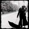 Black-and-white static icon showing a silhouetted couple embracing under an umbrella in a rainy park scene with trees and blurred background.