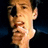 Pixelated close-up of a person's face with light skin tone, dark hair, and a neutral expression against a dark background.