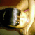 A pixelated close-up of a figure with closed eyes, wearing dark clothing and holding a glowing object against a warm-toned background.