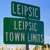 Green road signs with white text reading 'LEIPSC' on top and 'LEIPSC TOWN LOTS' below, set against a blue sky background.