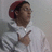 A person wearing a red cap and white hoodie points with their right hand while standing against a light gray background.
