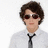 Pixelated image of a person with brown hair and sunglasses wearing a white shirt and black tie, set against blue background with text overlays.