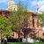Pixelated static image of a building with a domed roof, surrounded by greenery and a flagpole with a pink flag under a blue sky.