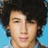 Pixelated close-up of a person with dark curly hair against a light blue background, showing facial features and partial neck.