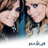 Two women with long wavy hair smile at the camera, one wearing a light blue top and the other a white top with a dangling earring, with 'mka' text at the bottom.