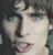 Static pixelated image of a person's face with light skin, dark hair, and blue eyes, cropped to show only the upper portion from forehead to chin.