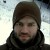 Pixelated static image of a person wearing a dark hooded garment against a light gradient background.