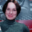 Static pixelated image of a person with dark hair wearing a teal turtleneck sweater against a blue-gray background with red accents.