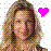 Pixelated image of a person with long brown hair and green highlights, wearing light-colored clothing, next to a bright pink heart symbol on white background.