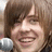 A pixelated image shows a person with brown hair holding a microphone, next to orange text reading 'simply amazing' on white background.