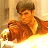 A pixelated figure with brown hair sits in a chair, holding a brown object, against a warm-toned background with light and dark vertical elements.