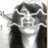 Pixelated grayscale image of a person in a suit with arms raised, wearing sunglasses and a white shirt, against a light background with a yellow vertical stripe on the right.
