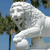 A pixelated image of a large white bear-like figure standing outdoors with green foliage and blue sky in the background.