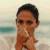 Pixelated image of a person with short dark hair holding hands near the face against a beach background with water and sand.