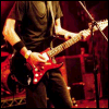 identical images showing a person playing red electric guitar on stage with dark clothing and microphone stands, each containing different text overlays
