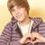 Pixelated image of a person with brown hair wearing a dark purple jacket over a white shirt, making a heart shape with hands against a light yellow background.