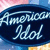 A pixelated oval-shaped icon with light blue text on a dark blue background, featuring stylized 'American Idol' lettering and a blurred colorful backdrop.