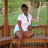 A pixelated image shows a person in a white shirt and brown shorts sitting on a wooden bench with green foliage in the background, next to a brown with white text reading "Pure Wickedness"