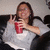 A pixelated image shows a person with long dark hair wearing a white top, holding up two fingers in a peace sign gesture while holding a red cup.