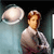 Pixelated image of a person with light brown hair wearing a white shirt, standing next to a large circular object against a gradient background.