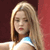 A pixelated close-up of a person with long blonde hair wearing a white top with a blue accent, set against a dark red background.