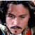Pixelated close-up of a person's face with dark hair, mustache, and visible red clothing against a dark background.