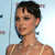 Pixelated close-up of a person with short dark hair, light skin, and a light-colored sleeveless top against a light blue background.