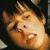Pixelated close-up of a person's face with light skin tone, dark hair, and closed eyes against a dark background.
