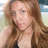 Pixelated close-up of a person with long brown hair wearing a light-colored top, set against a blurred background.