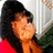 Pixelated static image of a person with dark hair wearing an orange top against a light background.