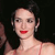 Pixelated close-up of a person with dark hair, red lips, and a light-colored strapless top against a dark background.
