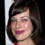 A static pixelated image shows a person with dark brown hair, light skin, and pink lips smiling slightly, with a white vertical element on the left side of the frame.