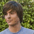 Pixelated image of a person with brown hair wearing a light blue shirt against a green foliage background.