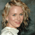 Pixelated close-up of a person with light brown curly hair wearing a white top against a dark gray background.