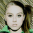 A pixelated image of a person with light brown hair tied back, wearing a dark choker and green clothing against a striped background, overlaid with blue text on bright green.