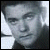 Pixelated grayscale portrait of a person with short dark hair, neutral expression, and light-colored clothing against a light background.