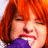 A person with short red hair and a purple garment covering their mouth, showing teeth in a tight expression across four