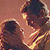 Two stylized figures in profile view, one larger with dark hair and light skin, the other smaller with dark hair and dark skin, both facing left against a brown background.