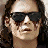 Pixelated close-up of a person with dark hair wearing dark sunglasses, light skin tone, and a neutral expression against a blurred background.