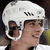 A static image shows a person wearing a white helmet with black ventilation slots and large circular ear protectors, set against a dark background.