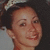 Pixelated close-up of a person with dark hair styled up, wearing light-colored earrings and red lipstick against a dark background.